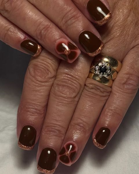Deep chocolate brown gel nails with copper glitter tips and a flower accent nail